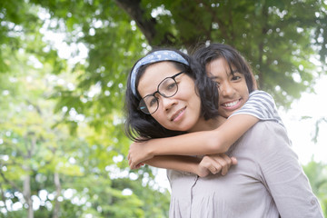 Naklejka premium Cute Asian mother and daughter playing and giving ride on back together at park, Happy family concept