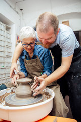 Senior woman spinning clay on a wheel with teacher at pottery class