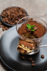Portion of Classic tiramisu dessert in a glass cup on concrete background