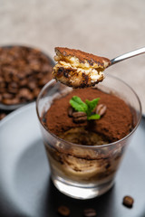 Portion of Classic tiramisu dessert in a glass cup on concrete background