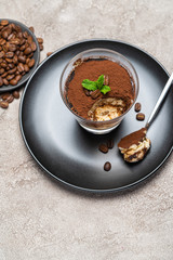 Portion of Classic tiramisu dessert in a glass cup on concrete background
