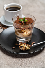 Portion of Classic tiramisu dessert in a glass cup and espresso coffee on concrete background
