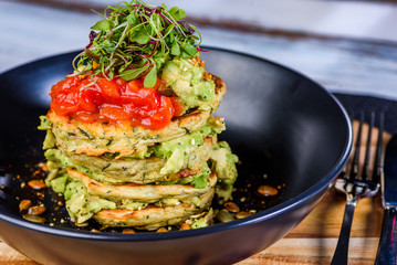 A dish of vegetable patties, Halloumi and Avocado, stacked up on a dark blue plate.