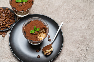 Portion of Classic tiramisu dessert in a glass cup on concrete background