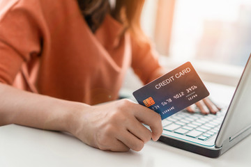 Young asian woman holding mockup credit card and use laptop for purchase product on internet in home office, Cyber Monday shopping online concept, Copy space.