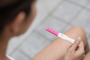 Young asian woman holding pregnancy test showing a positive result in bathroom, Wellness and healthy concept, Abortion problem, Selective focus.