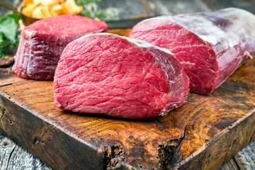 Dry aged Rinderfilet Steak Medaillons natur angeboten als closeup mit Pfifferlingen auf einem rustikalen alten Schneidebrett