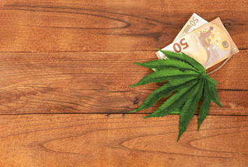 Cannabis leaf and euro banknotes on the wood table, flat lay