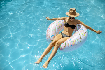 Woman in swimsuit and hat swimming with inflatable ring in the form of a donut in the water pool, view from above