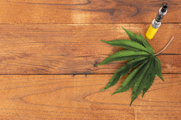 Marijuana/Cannabis leaf with electronic cigarette on wooden background, copy space. Flat lay