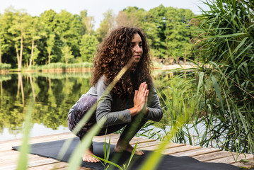 Piękna kobieta ćwiczy jogę w parku nad jeziorem.  - obrazy, fototapety, plakaty