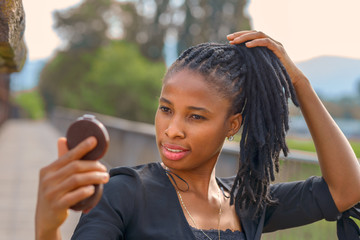 Stylish young African woman checking her face
