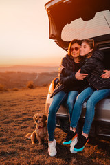 Daughter embracing mother while sitting in car trunk