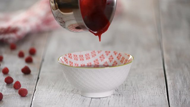 Woman pouring raspberries jam in a bowl.