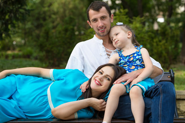 Family sitting on a bench in park. Woman pregnant. Happy family life concept.