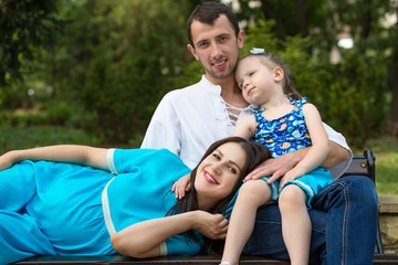 Fototapeta premium Family sitting on a bench in park. Woman pregnant. Happy family life concept.