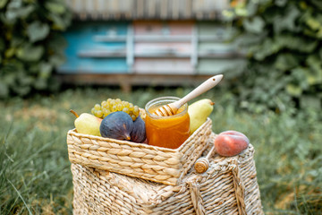 Composition of sweet fruits and jar full of honey with woooden beehives on the background at the apiary