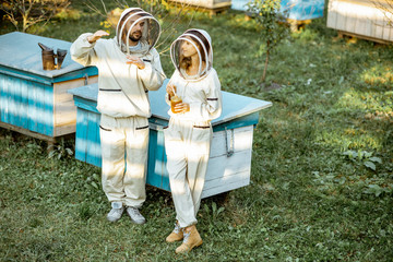 Two beekeepers in protective uniform standing together near the wooden beehives on a small traditional apiary. Concept of beekeeping and small farming