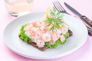 Traditional savory swedish sandwich with dark bread, lettuce, eggs, mayonnaise, shrimps, dill and lemon, on pink background, horizontal