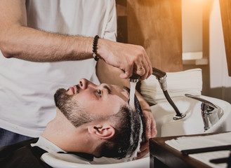 Young man with trendy haircut at barber shop. Barber washes customer head.