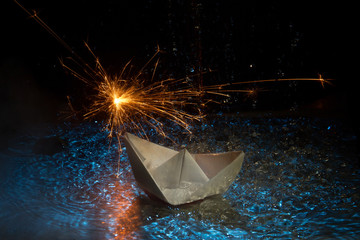 paper boat sailing on blue water in the raging sea. Around the spray of water, night, sparklers...