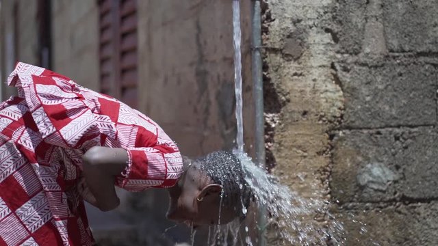 Beautiful African Girl Washes Her Head under Fresh Clean Water from a tap outdoors in Bamako, Mali.