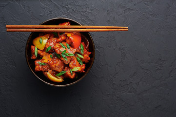 Chicken Manchurian in bowl at black concrete background. Chicken Manchurian is Indian Chinese cuisine dish with Chicken breasts, bell pepper, tomatoes, soy sauce. Copy space