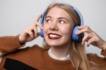 Naklejka premium Happy young blonde female with bright red lips enjoying favorite song while listening it on headphones. Using earphones