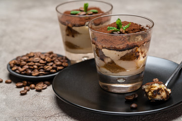 Portion of Classic tiramisu dessert in a glass cup on concrete background