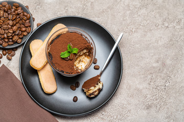 Portion of Classic tiramisu dessert in a glass cup on concrete background