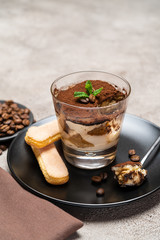 Portion of Classic tiramisu dessert in a glass cup on concrete background