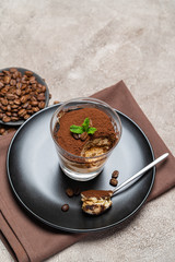 Portion of Classic tiramisu dessert in a glass cup on concrete background