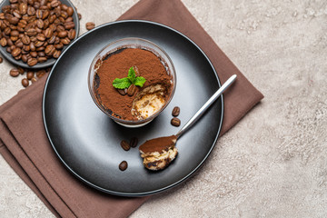 Portion of Classic tiramisu dessert in a glass cup on concrete background
