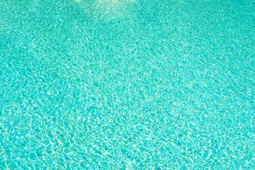 Fototapeta na wymiar Background of water in blue swimming pool, water surface with a sun reflection