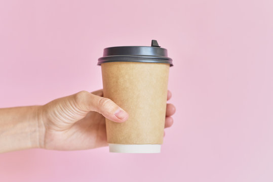 Mockup of female hand holding coffee paper cup on pink background.