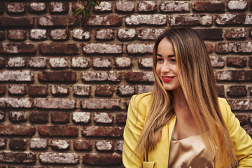 Portrait of a young beautiful laughing woman with long hair  and a yellow jacket against the background of a brick wall on a cloudy day. Close-up,