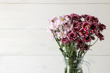 Bouquet of autumn flowers of pink chrysanthemums in a jug on a light wooden background