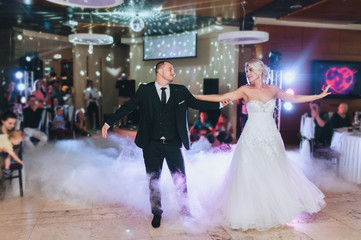 Loving newlyweds dance in the evening restaurant at a party with smoke. Wedding dance of a stylish groom and a beautiful bride. Concept and photography.