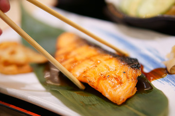 delicious teppanyaki salmon steak food for omega 3 and wood chopsticks with vegetable and sauce on green leaf and white dish with table at japanese restaurant for lunch or healthy dinner