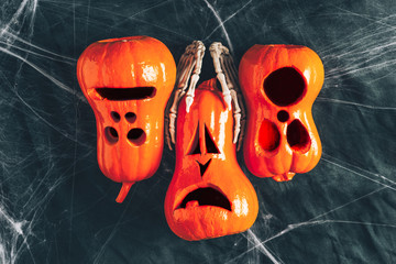 Halloween background, pumpkins with eyes and mouths cut out, Bony hands hugging a pumpkin ,Jack lamp, gloomy and dark atmosphere, stretched web in the background