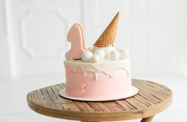 pink girl’s cake for a year, decorated with mastic balls and a waffle cone on table