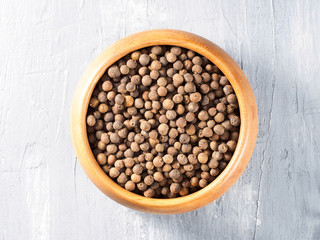 Allspice (Jamaica pepper) in a wooden cup on a gray background