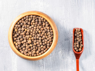 Allspice (Jamaica pepper) in wooden cup and scoop on a gray background with stains