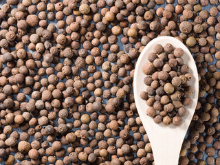 Allspice (Jamaica pepper) in a wooden spoon on allspice background
