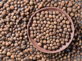 Allspice (Jamaica pepper) in a clay plate on allspice background