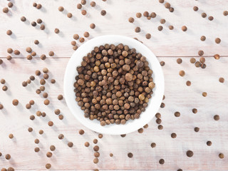 Allspice (Jamaica pepper) in a white cup on a wooden brown background
