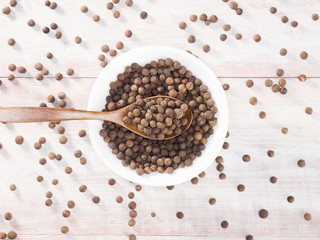 Allspice (Jamaica pepper) in a white cup and spoon on a brown wooden background