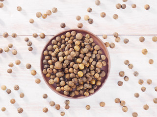 Allspice (Jamaica pepper) in a clay plate on a brown wooden background
