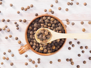 Allspice (Jamaica pepper) in a clay cup and wooden spoon on a brown wooden background