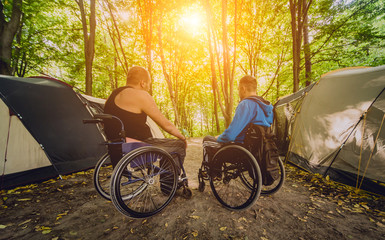 Two disabled men resting in a campsite with friends. Wheelchair in the forest on the background of...